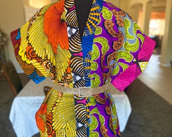 May include: A short-sleeved kimono-style jacket featuring a vibrant patchwork of African-inspired prints in orange, yellow, purple, and green. The garment is cinched at the waist with a thin, sparkling silver rhinestone belt.