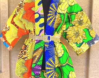 Op de afbeelding: Een jas in kimonostijl met een levendige patchwork van Afrikaans geïnspireerde prints in tinten geel, oranje, groen en blauw. Het kledingstuk is in de taille ingesnoerd met een dunne, glinsterende goudkleurige riem met een vierkante gesp.