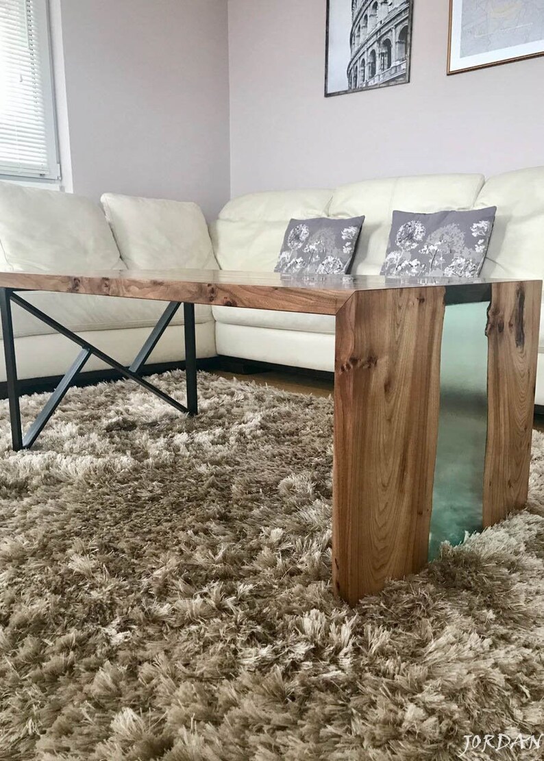May include: A wooden coffee table with a clear epoxy resin inlay. The table has a black metal X-shaped base and sits on a brown shag rug.