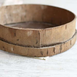 May include: A round wooden sifter with a woven wire mesh bottom. The sifter is made of natural wood and has a rustic, vintage look.