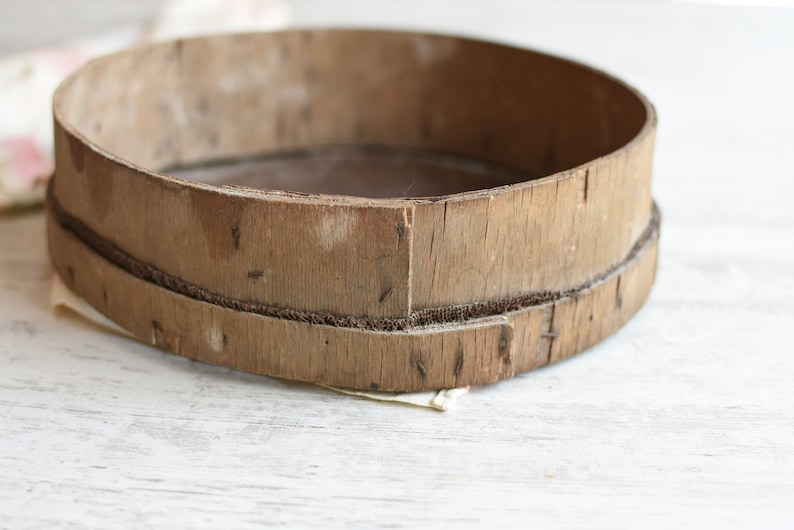 May include: A round wooden sifter with a woven wire mesh bottom. The sifter is made of natural wood and has a rustic, vintage look.