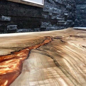Pu&ograve; includere: Primo piano di un piano da tavolo in legno con una venatura del legno naturale. Un fiume di resina arancione scorre al centro del tavolo.