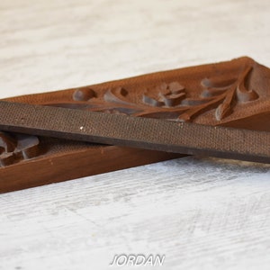 May include: A vintage woodworking rasp and a carved wooden tray. The rasp is a dark brown color with a textured surface. The tray is also brown and features carved floral and leaf designs. The rasp is approximately 10 inches long.
