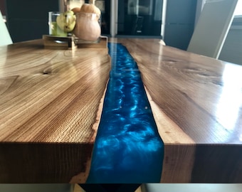 May include: A wooden table with a blue epoxy resin river running down the centre. The table has a natural wood finish and is polished to a high shine.