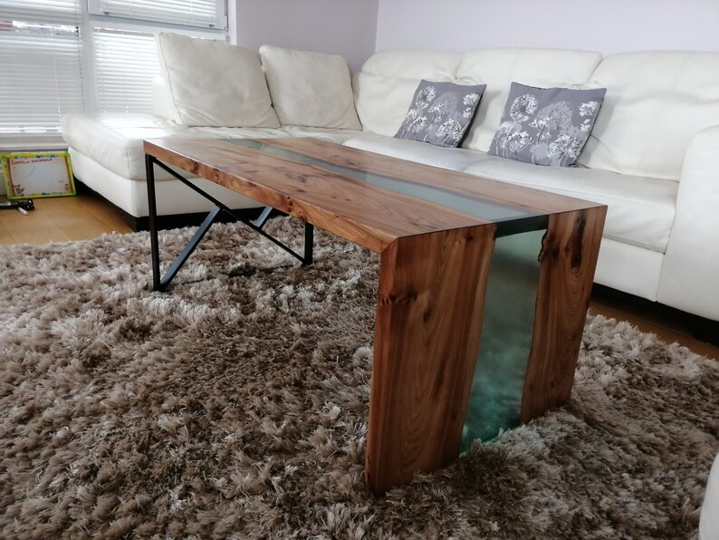 May include: A wooden coffee table with a clear epoxy river running through the center. The table has a black metal frame and is sitting on a brown shag rug.