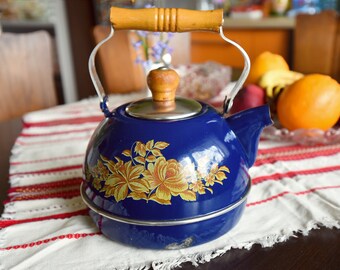 May include: A blue enamel teapot with a floral design and a wooden handle. The teapot is sitting on a white and red striped tablecloth.