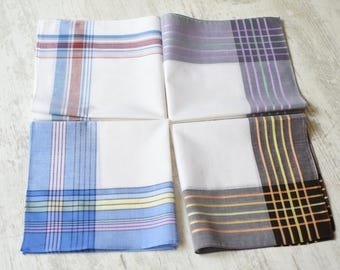 May include: Four square cotton handkerchiefs arranged in a grid. Each features a white base with distinct corner patterns: one with blue and red stripes, one with purple and green checks, one with blue and yellow lines, and one with black and orange grids.