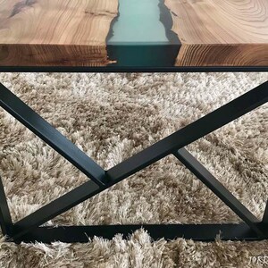 May include: A wooden table top with a teal epoxy river running through it. The table has a black metal base with a geometric design.