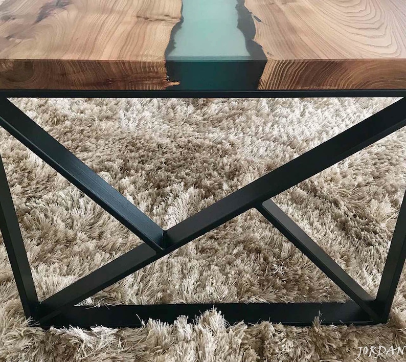 May include: A wooden table top with a teal epoxy river running through it. The table has a black metal base with a geometric design.