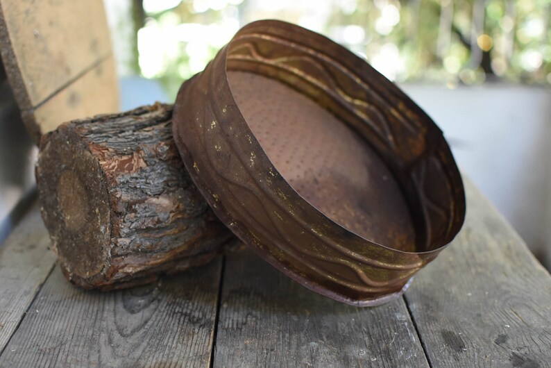 Puede incluir: Una bandeja redonda de metal oxidado con un borde decorativo. La bandeja est&aacute; sentada sobre un trozo de madera.