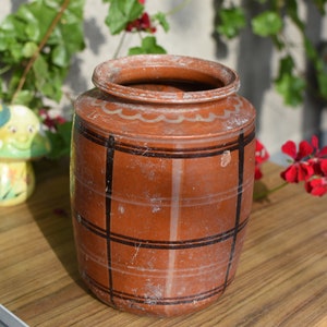 Peut inclure: Un pot en céramique brun avec un motif en damier noir et blanc. Le pot a une large ouverture et un corps arrondi. Il est posé sur une table en bois.