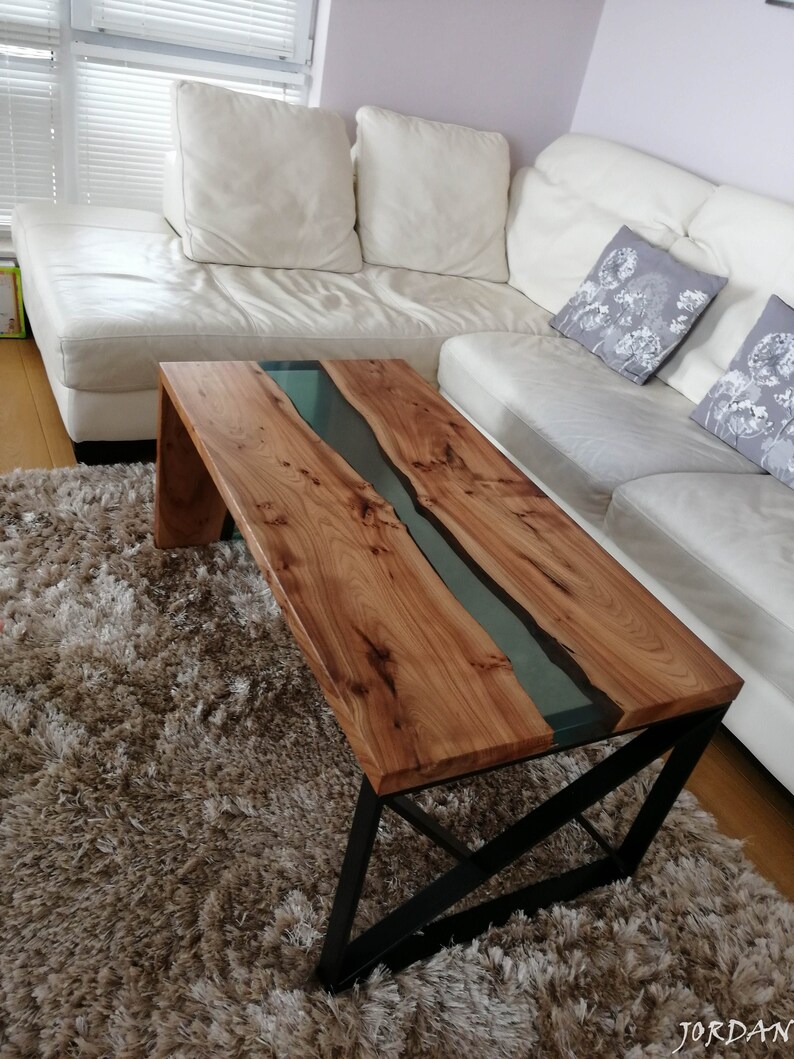 May include: A wooden coffee table with a black metal frame. The table top has a natural wood finish with a clear epoxy river running through the center.