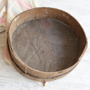 May include: A round wooden sifter with a mesh screen. The sifter is made of natural wood and has a rustic, vintage look.