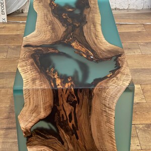 May include: A wooden coffee table with a teal blue epoxy resin inlay. The wood has a natural grain pattern and the resin is smooth and glossy.