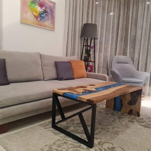 May include: A modern living room with a gray sofa, a gray armchair, and a coffee table with a blue epoxy resin river inlay. The table has a black metal frame.