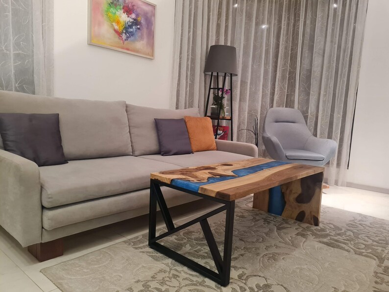 May include: A modern living room with a gray sofa, a gray armchair, and a coffee table with a blue epoxy resin river inlay. The table has a black metal frame.