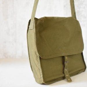 May include: A green canvas messenger bag with a flap closure and a buckle strap. The bag has a worn look and is made of a durable material.
