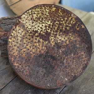 Puede incluir: Una cabeza de regadera redonda de metal oxidada con un acabado de pintura dorado y un patr&oacute;n de peque&ntilde;os agujeros. La cabeza de la regadera est&aacute; sobre una superficie de madera.