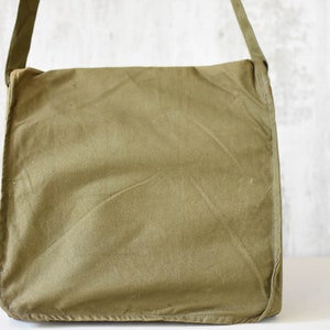 May include: A green canvas messenger bag with a long adjustable strap. The bag has a flap closure and a simple design.