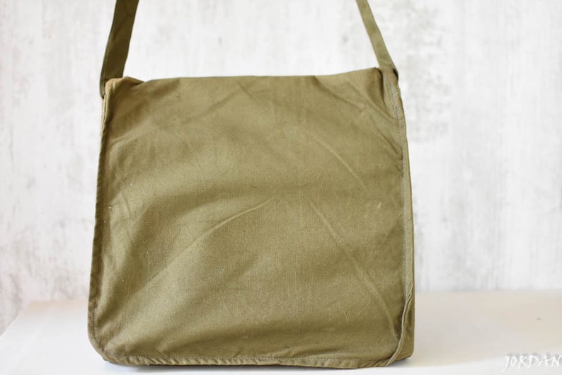 May include: A green canvas messenger bag with a long adjustable strap. The bag has a flap closure and a simple design.