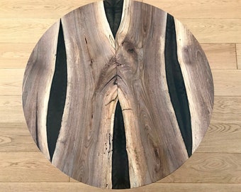 May include: Round wooden table top with black resin inlay. The wood has a natural grain pattern and the resin is smooth and glossy.