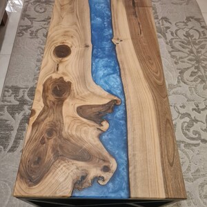 May include: A wooden coffee table with a blue resin river running through the center. The table has a black geometric base.