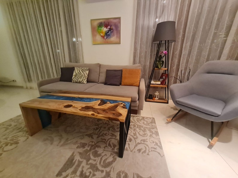 May include: A living room with a gray couch, a gray armchair, a wooden coffee table with a blue resin river, and a floor lamp with a black shade.