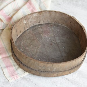 May include: A round wooden sifter with a wire mesh bottom. The sifter is made of natural wood and has a rustic, vintage look.