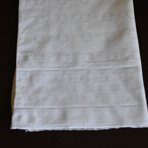 May include: White cotton fabric with a delicate embroidered pattern of small flowers and circles. The fabric has a smooth texture and a slightly sheer appearance.