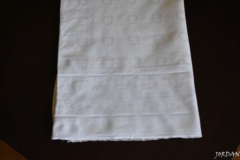 May include: White cotton fabric with a delicate embroidered pattern of small flowers and circles. The fabric has a smooth texture and a slightly sheer appearance.