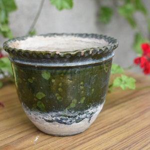 Puede incluir: Una maceta de cerámica verde glaseada con un borde blanco y una superficie texturizada. La maceta tiene un borde festoneado y es perfecta para plantas de interior.