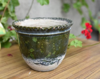 May include: A green glazed ceramic planter with a white rim and a textured surface. The planter has a scalloped edge and is perfect for indoor plants.