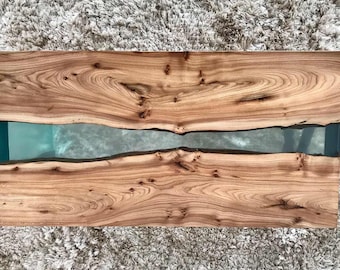 Puede incluir: Una tapa de mesa de madera con un acabado de veta de madera natural. La tapa de mesa tiene una grieta larga y estrecha llena de resina epoxi transparente.