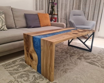 Puede incluir: Una mesa de centro de madera con un río de resina azul que fluye por el centro. La mesa tiene un marco de metal negro y está sentada sobre una alfombra estampada.