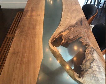 May include: A wooden dining table with a live edge and a clear epoxy river running down the center. The table is surrounded by black chairs.