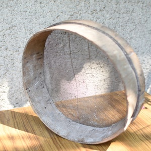 May include: A round wooden sieve with a woven mesh bottom. The sieve is made of light brown wood and has a natural finish. It is sitting on a wooden table.