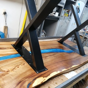 May include: A wooden table top with a blue epoxy river running through it. The table has a black metal X-shaped base.