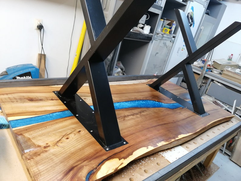 May include: A wooden table top with a blue epoxy river running through it. The table has a black metal X-shaped base.