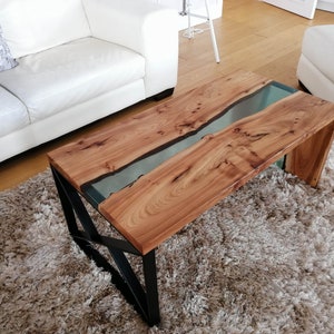 May include: A wooden coffee table with a clear epoxy river running through the center. The table has a black metal frame and is sitting on a fluffy rug.