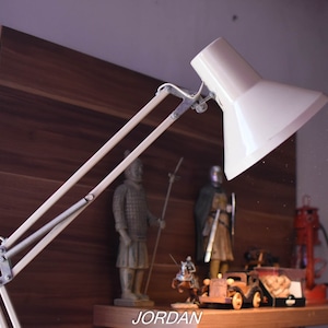 May include: A white adjustable desk lamp with a long arm and a white shade. The lamp is positioned over a shelf with various decorative items, including figurines and a small car.