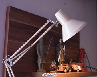 May include: A white adjustable desk lamp with a long arm and a white shade. The lamp is positioned over a shelf with various decorative items, including figurines and a small car.