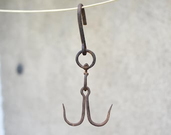 May include: A dark brown, weathered iron meat hook featuring a large top hook connected to a central ring, which attaches to a swivel mechanism and a double-pronged bottom hook. The metal surface shows signs of oxidation and age-related wear.