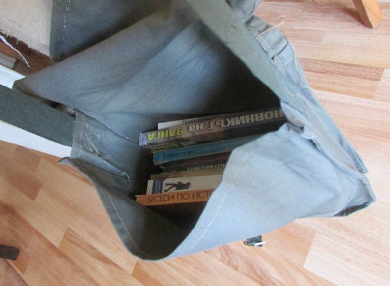 May include: A gray canvas bag with a zipper closure and a strap. The bag is filled with several books, including one with the title "BAHIA" in Russian.