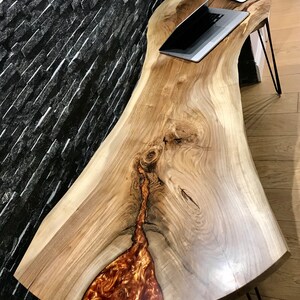Pu&ograve; includere: Una scrivania in legno a bordo vivo con una finitura in legno naturale e un grande inserto in resina di colore rame. La scrivania ha una forma curva ed &egrave; sostenuta da gambe a forcina.