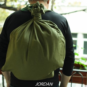 May include: A person wearing a black shirt is carrying a large, green canvas bag on their back. The bag is tied at the top with a green cord.