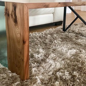 May include: A close-up of a wooden table leg with a clear epoxy resin inlay. The table leg is resting on a light brown shag rug.