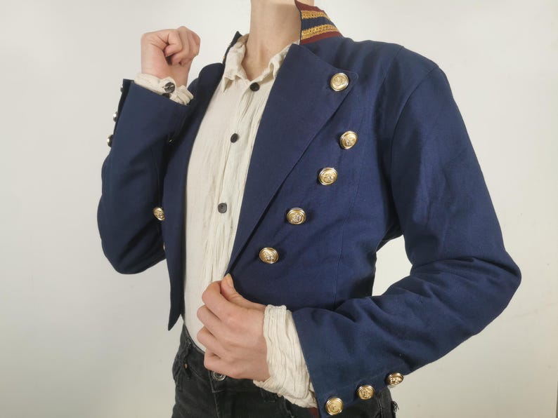 May include: A navy blue cropped jacket with gold buttons and a red and gold trim around the collar.