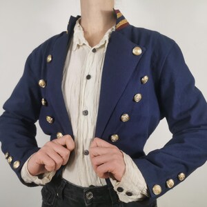 May include: A navy blue cropped jacket with gold buttons and a white collared shirt underneath.