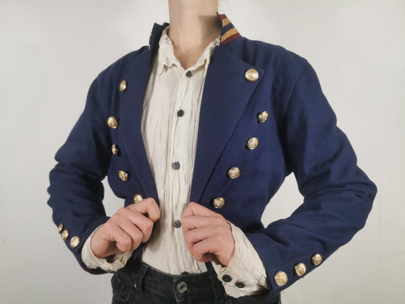 May include: A navy blue cropped jacket with gold buttons and a white collared shirt underneath.