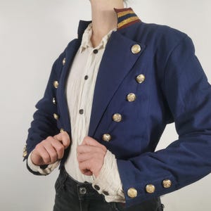 May include: A navy blue cropped jacket with gold buttons and a gold and red striped collar.